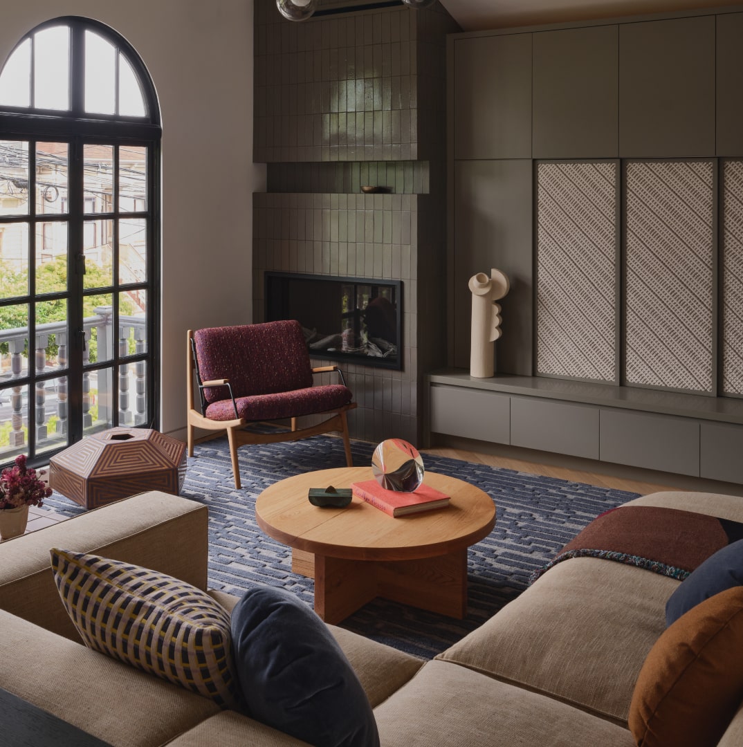 Modern living room with large arched window, beige sectional sofa, round wooden coffee table, purple armchair, and a fireplace.