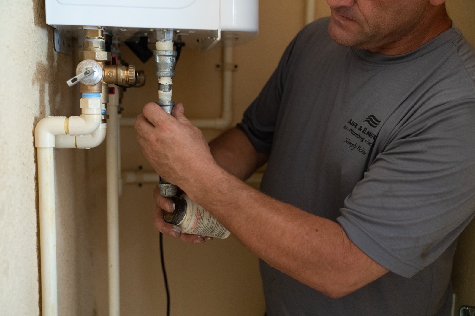 An Air & Energy plumber working on the water connections beneath a tankless water heater in a home's equipment closet.