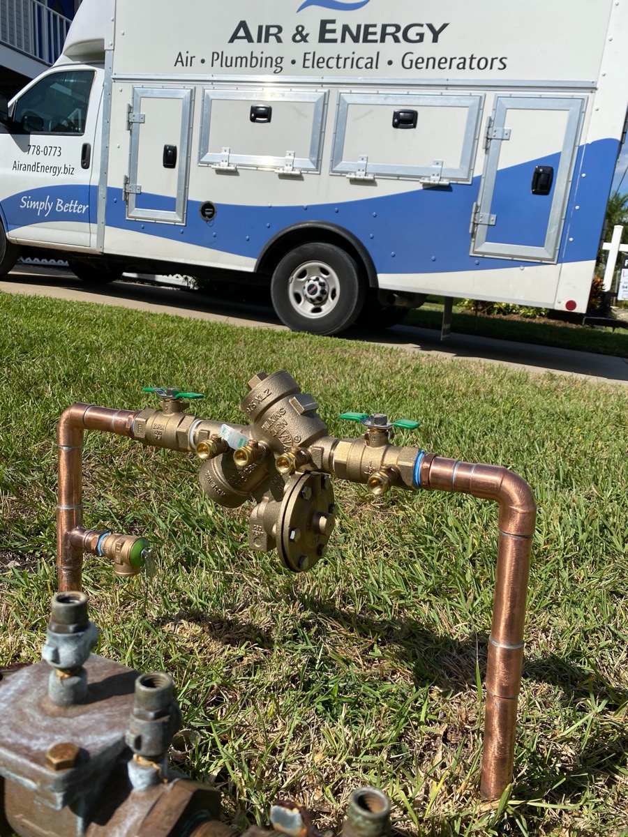 New brass backflow preventer on copper pipe in a lawn, with an Air & Energy truck behind it