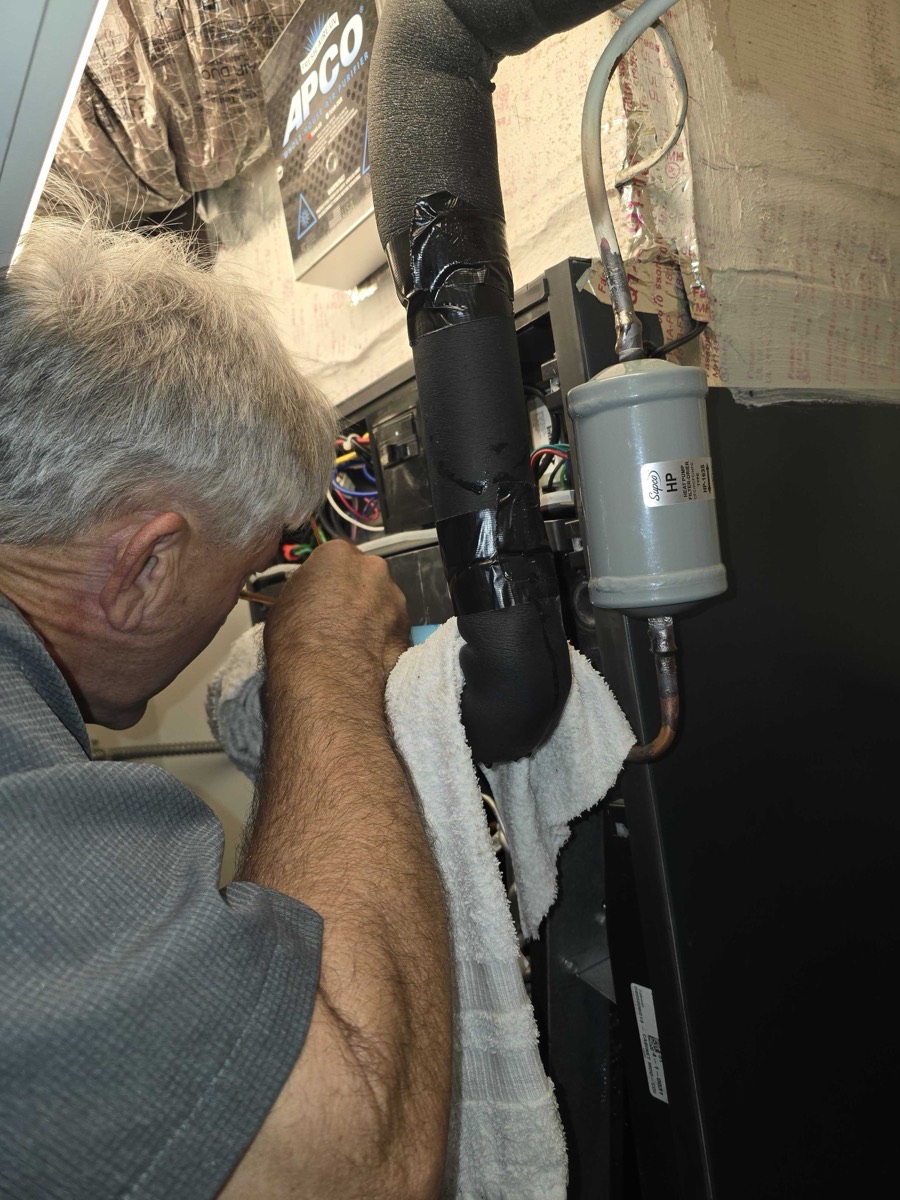 Air & Energy technician working inside an indoor air handler next to a heat pump filter drier