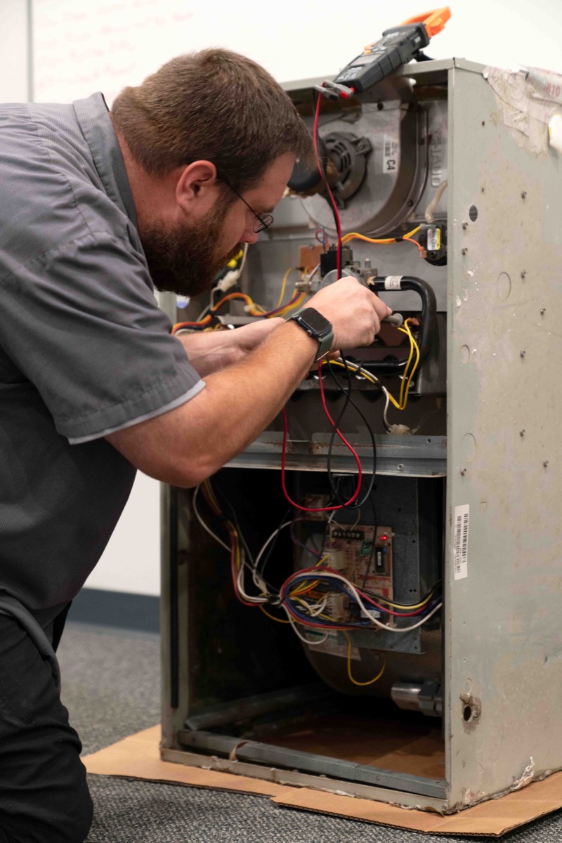 Air & Energy technician testing the controls of a gas furnace with a meter during training