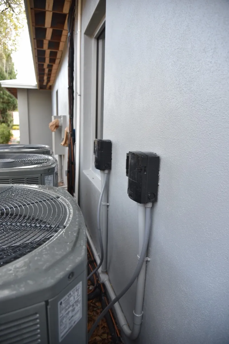 New Trane outdoor AC units lined up along a house wall, with disconnect boxes mounted on the wall beside them