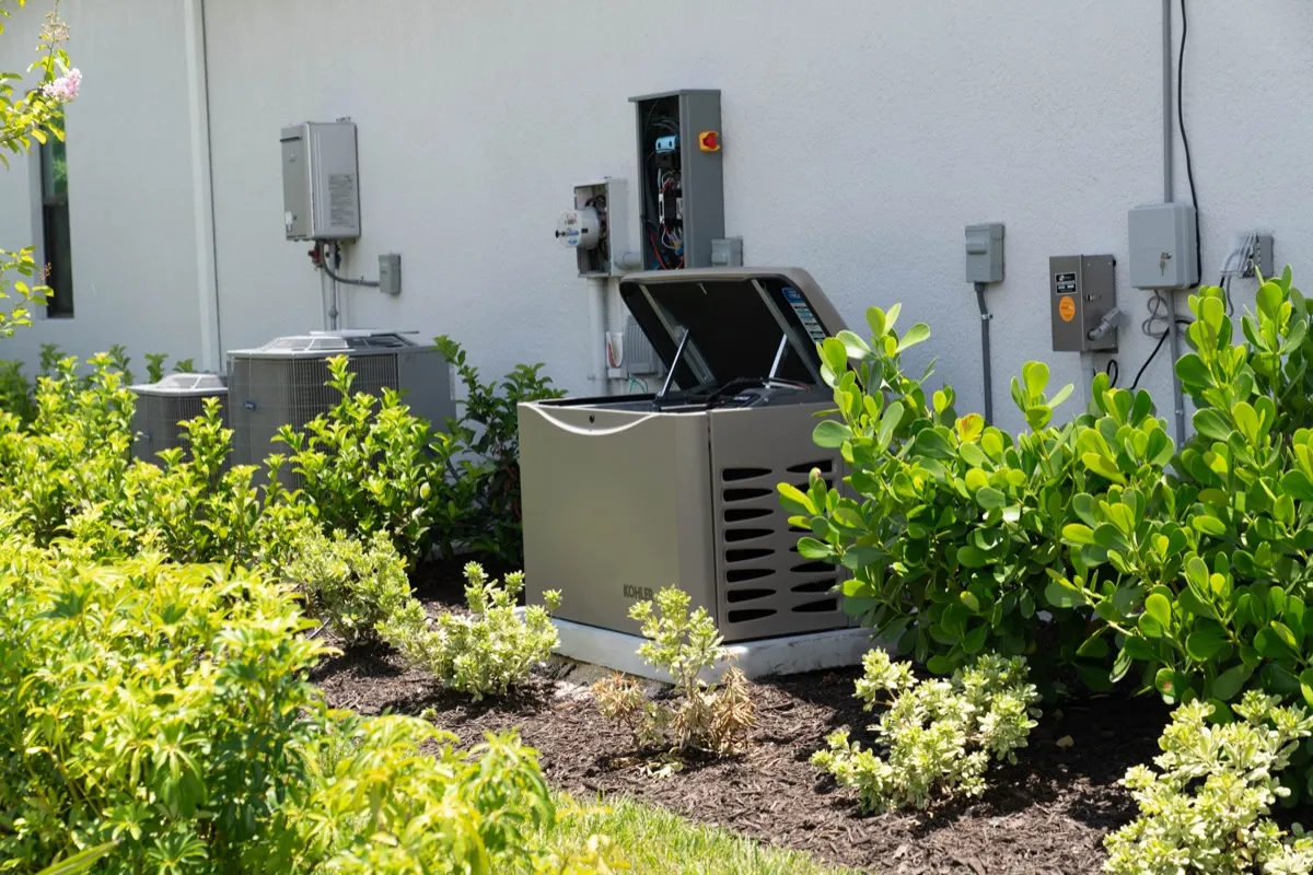 A newly installed Kohler home standby generator on its pad beside a house, lid open, with the transfer switch and electric meter on the wall behind it
