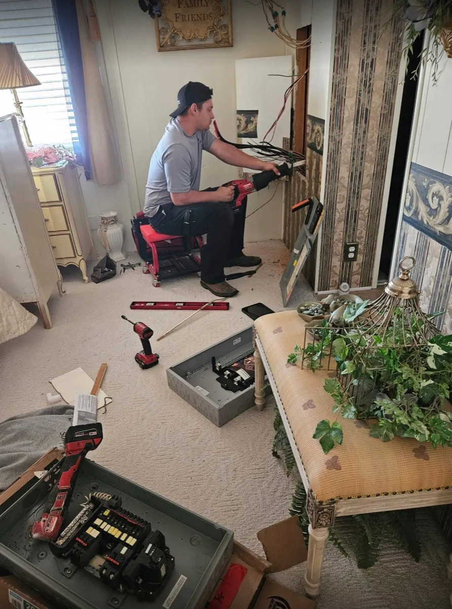 An Air & Energy electrician cutting out an old electrical panel inside a home, with the new panel box on the floor beside him