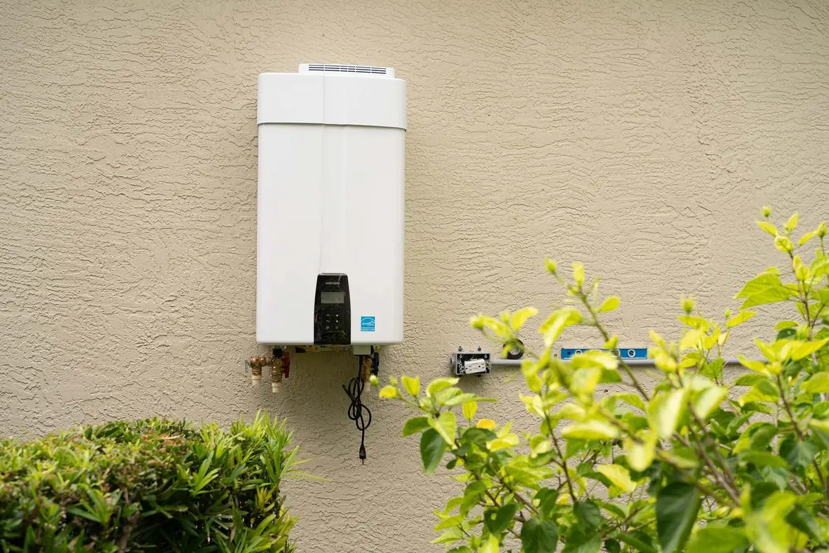 Newly installed tankless water heater mounted on the stucco wall of a home, with shutoff valves and a new electrical box beside it