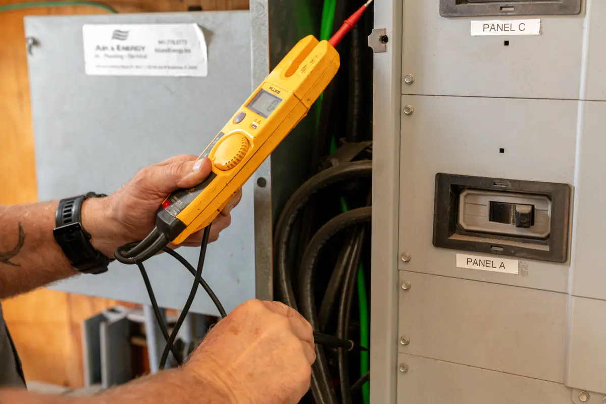 Close-up of an Air & Energy electrician testing an electrical panel with a voltage tester