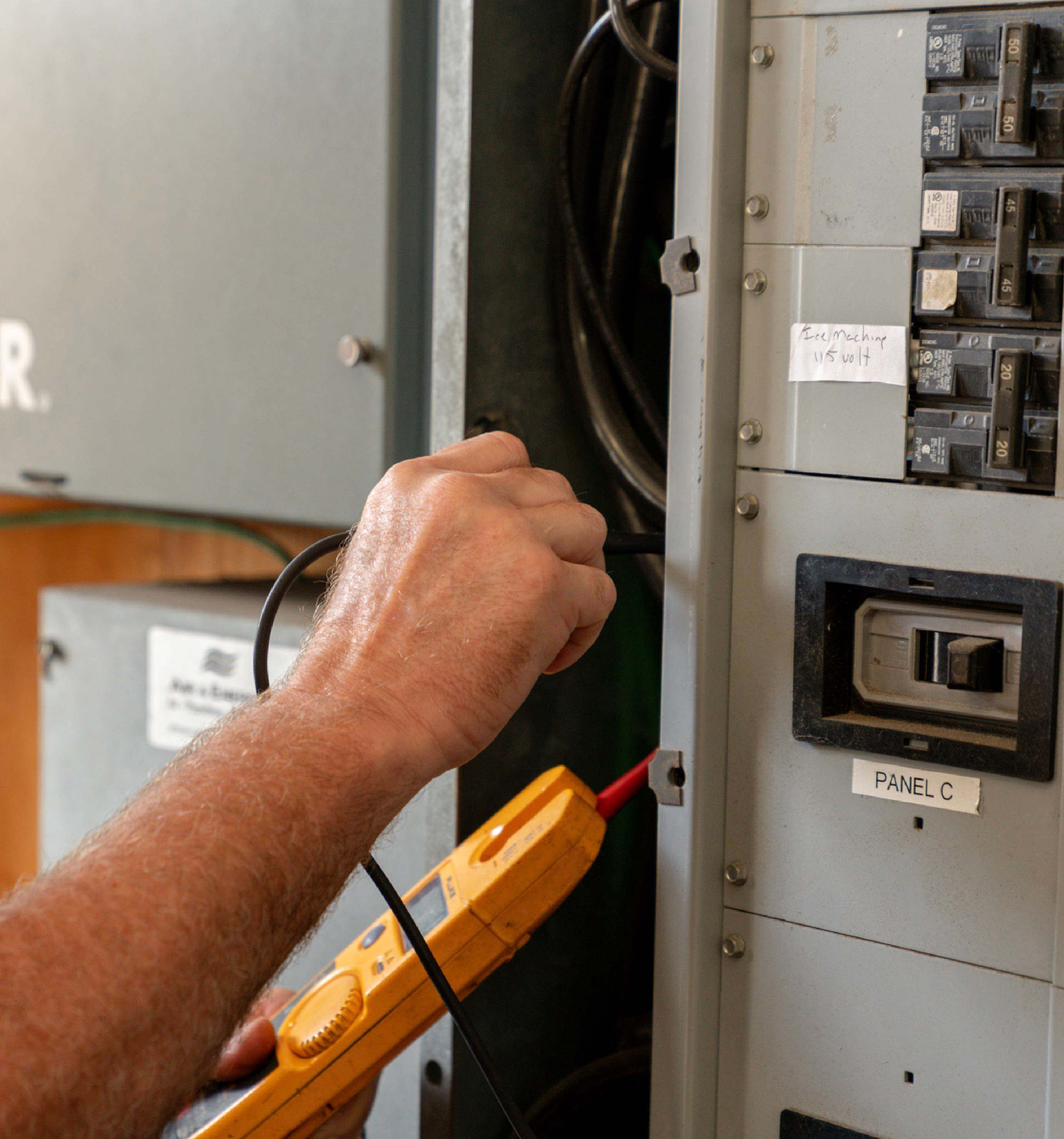 Close-up of a person using a yellow multimeter to test a circuit breaker in electrical panel C.