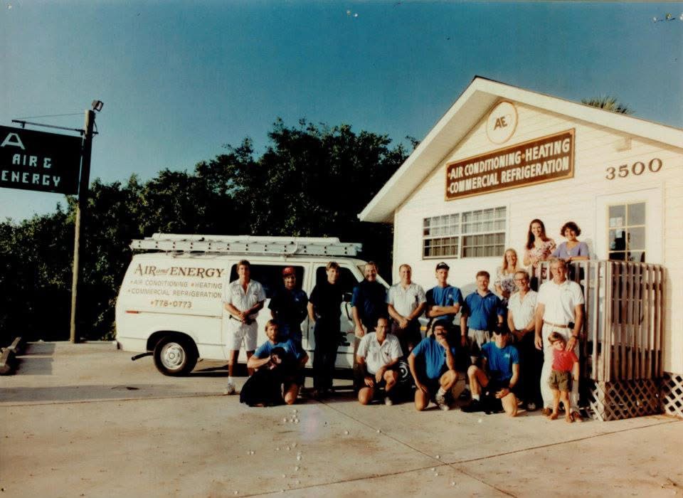 Group of men, women, and a child posing outside a white commercial building with an Air Energy van and signage for air conditioning, heating, and refrigeration.