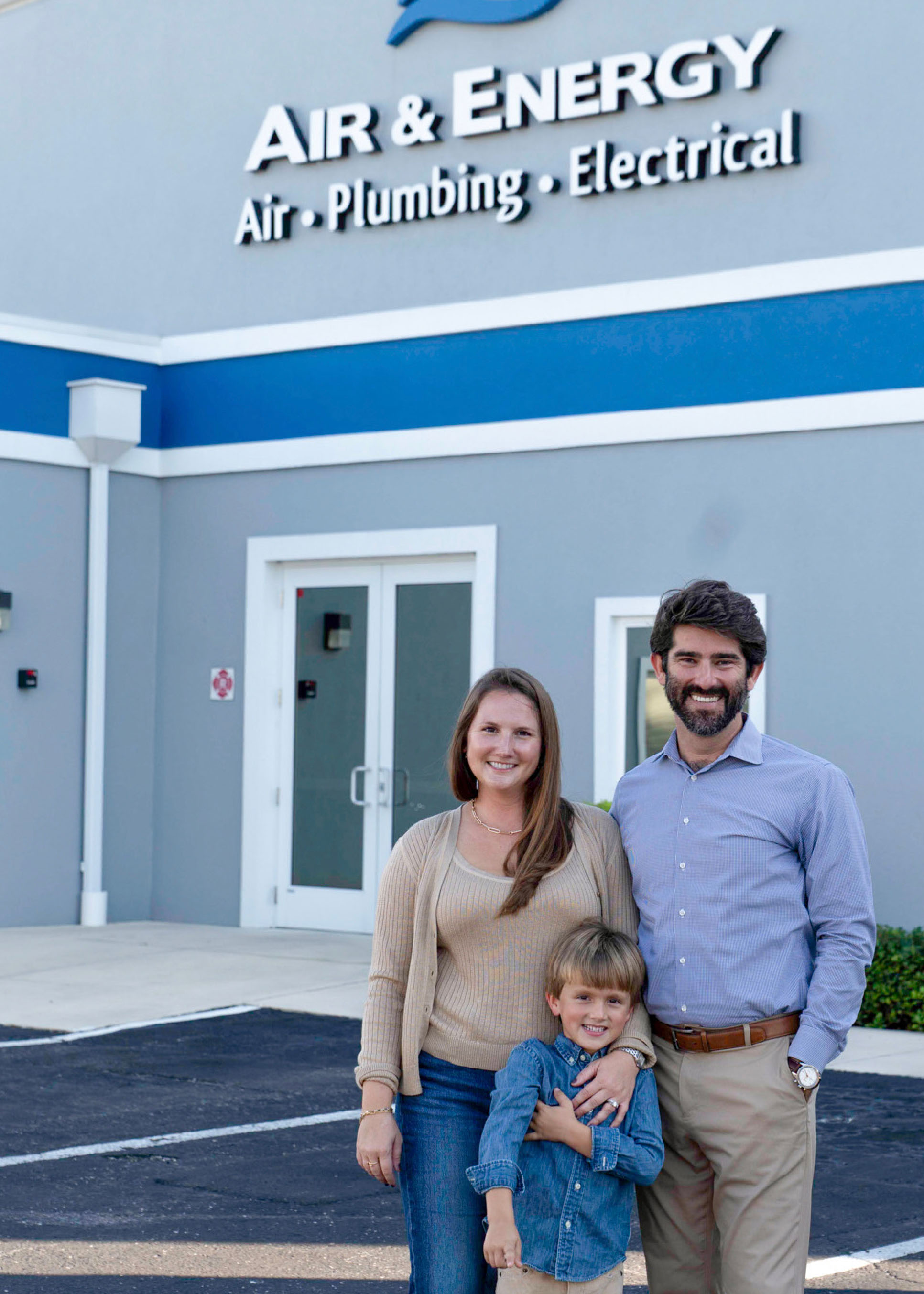 Moon family of three smiling and standing in front of a building with Air & Energy signage.