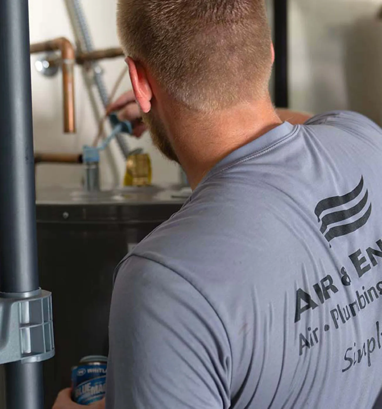 An Air & Energy plumber in a company shirt working beside a water heater