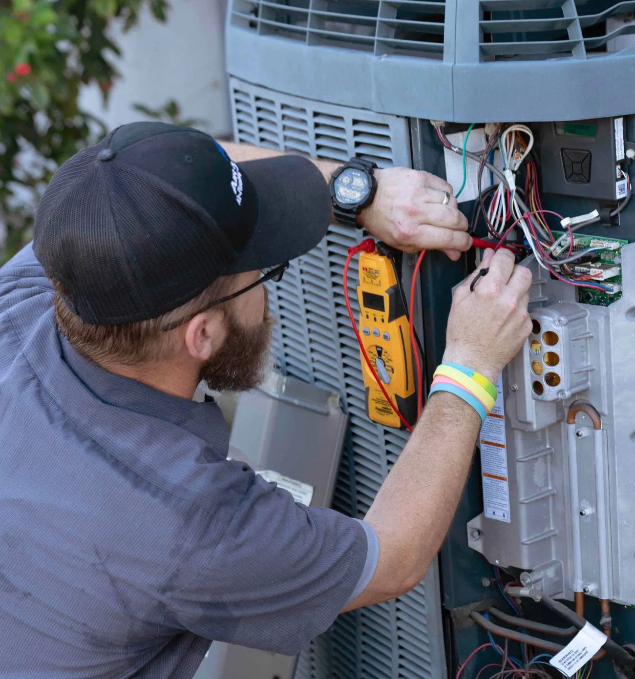 An Air & Energy technician testing the wiring of an outdoor air conditioning unit with a multimeter