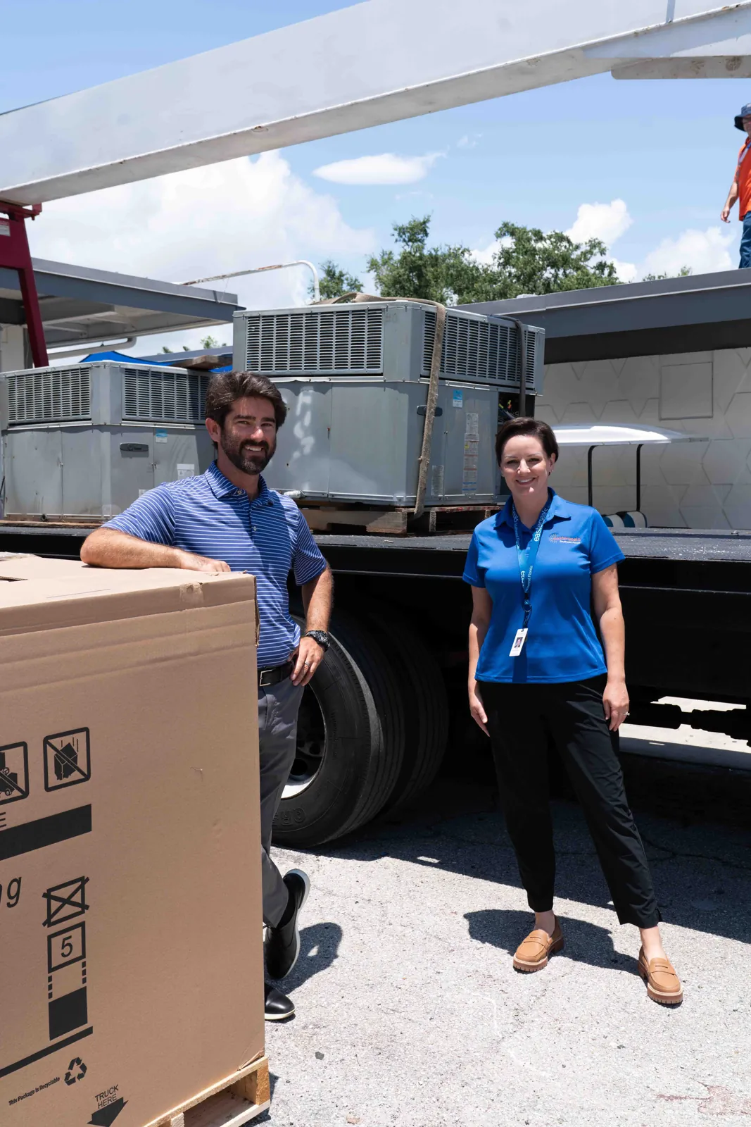 Two people stand beside a flatbed truck carrying rooftop air conditioning units at Easterseals Southwest Florida