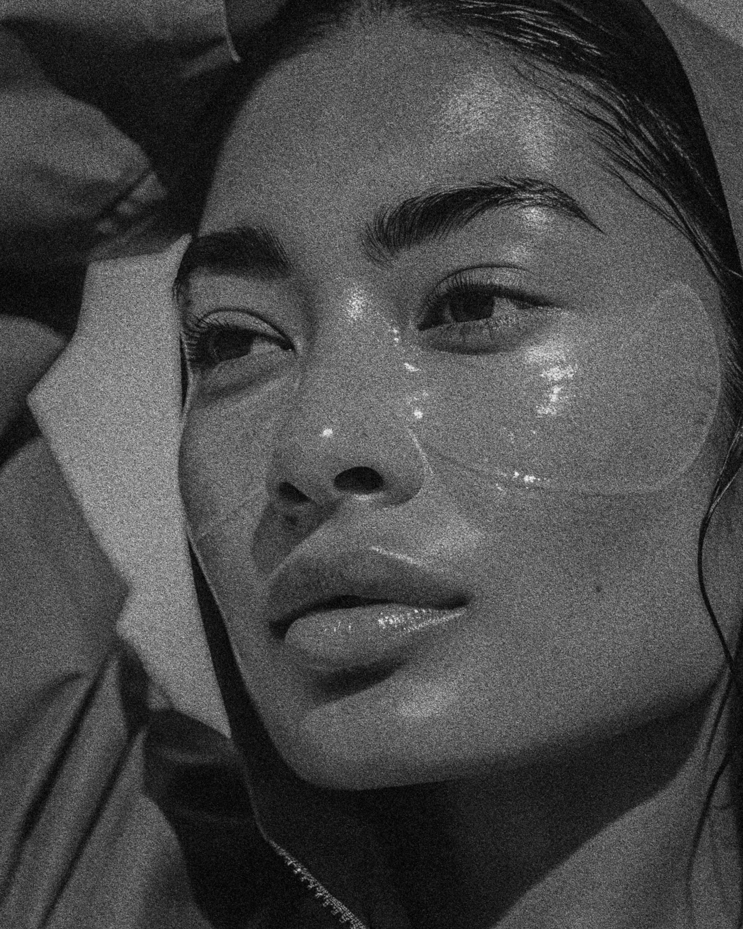 Close-up black and white portrait of a woman with shiny skin and a contemplative expression.