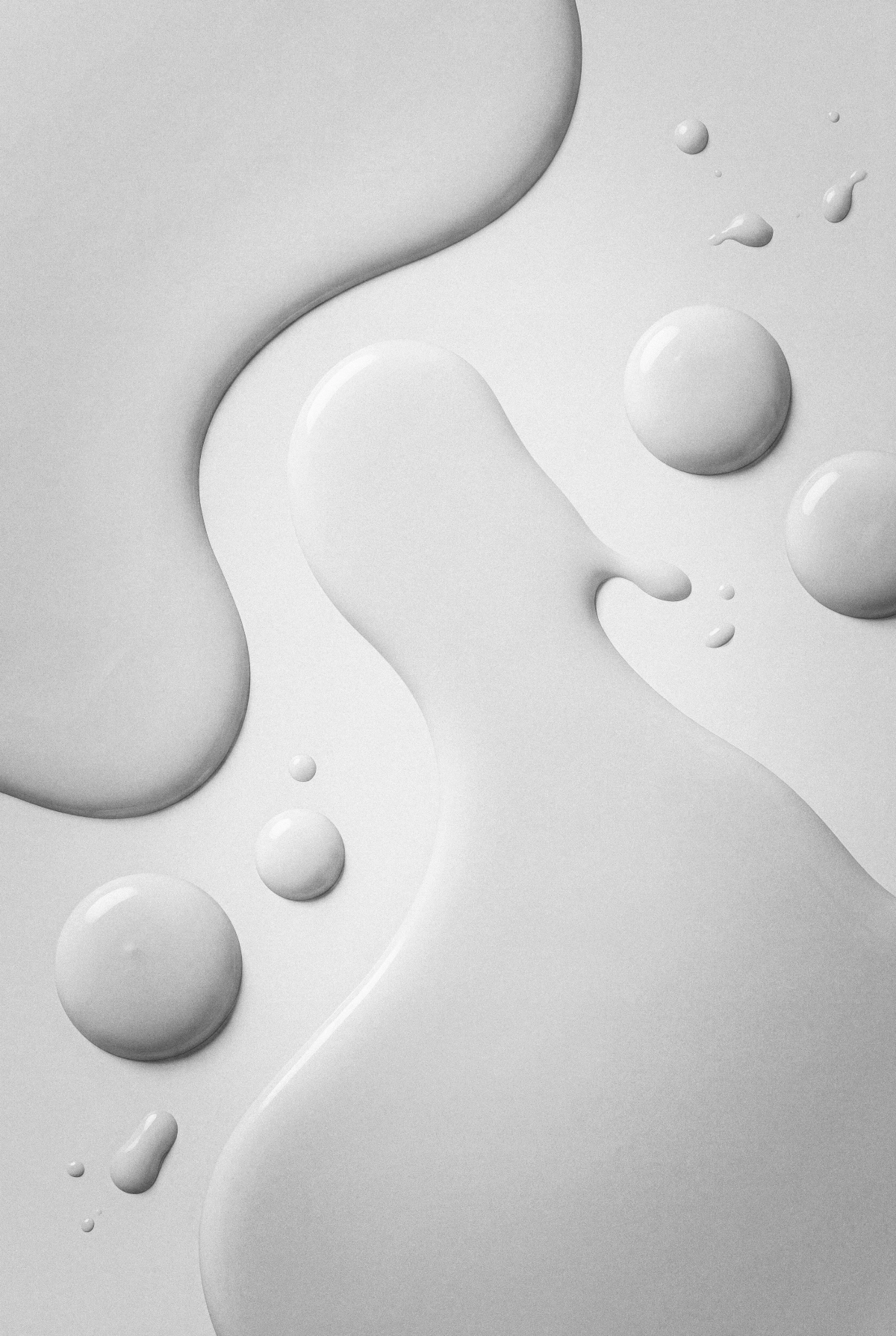Close-up of various droplets of white liquid on a flat surface with soft shadows and highlights.