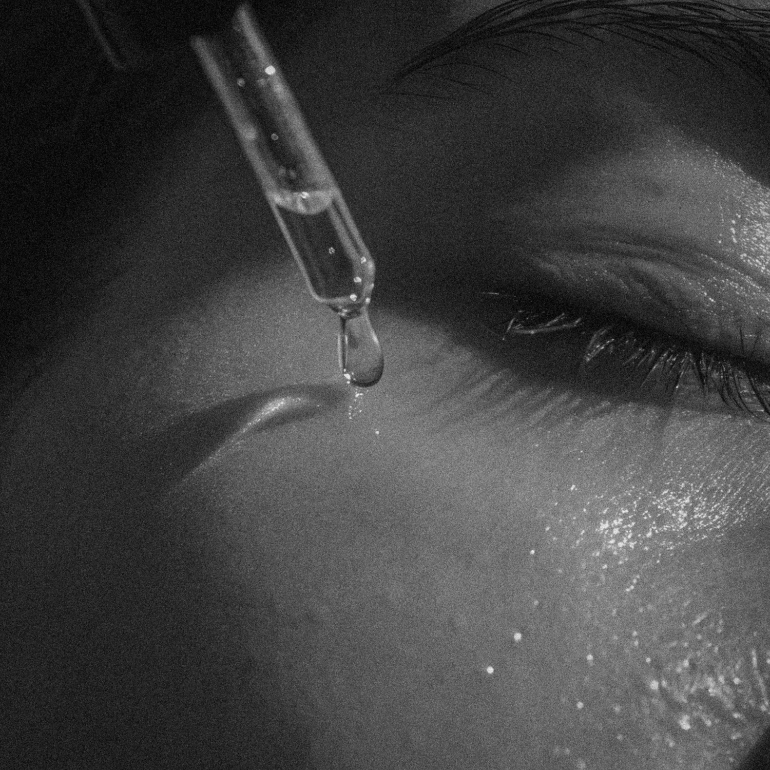 Close-up of a dropper releasing a serum drop onto a person's smooth cheek near a closed eye with long eyelashes.