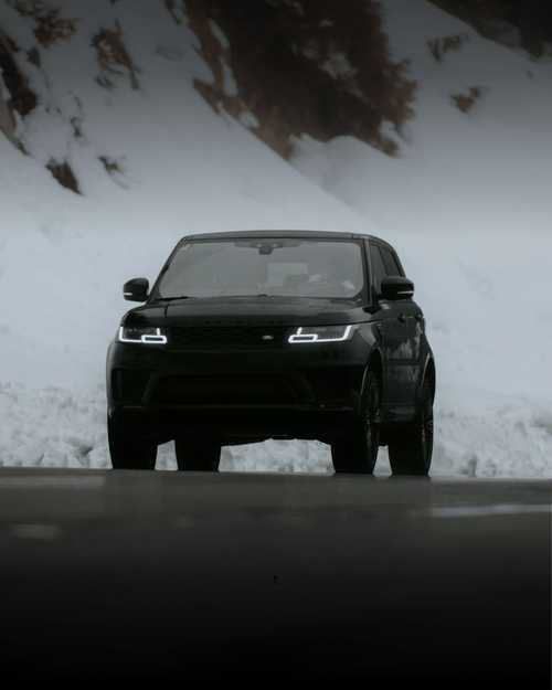 Black Range Rover SUV with headlights on driving on a snowy mountain road.