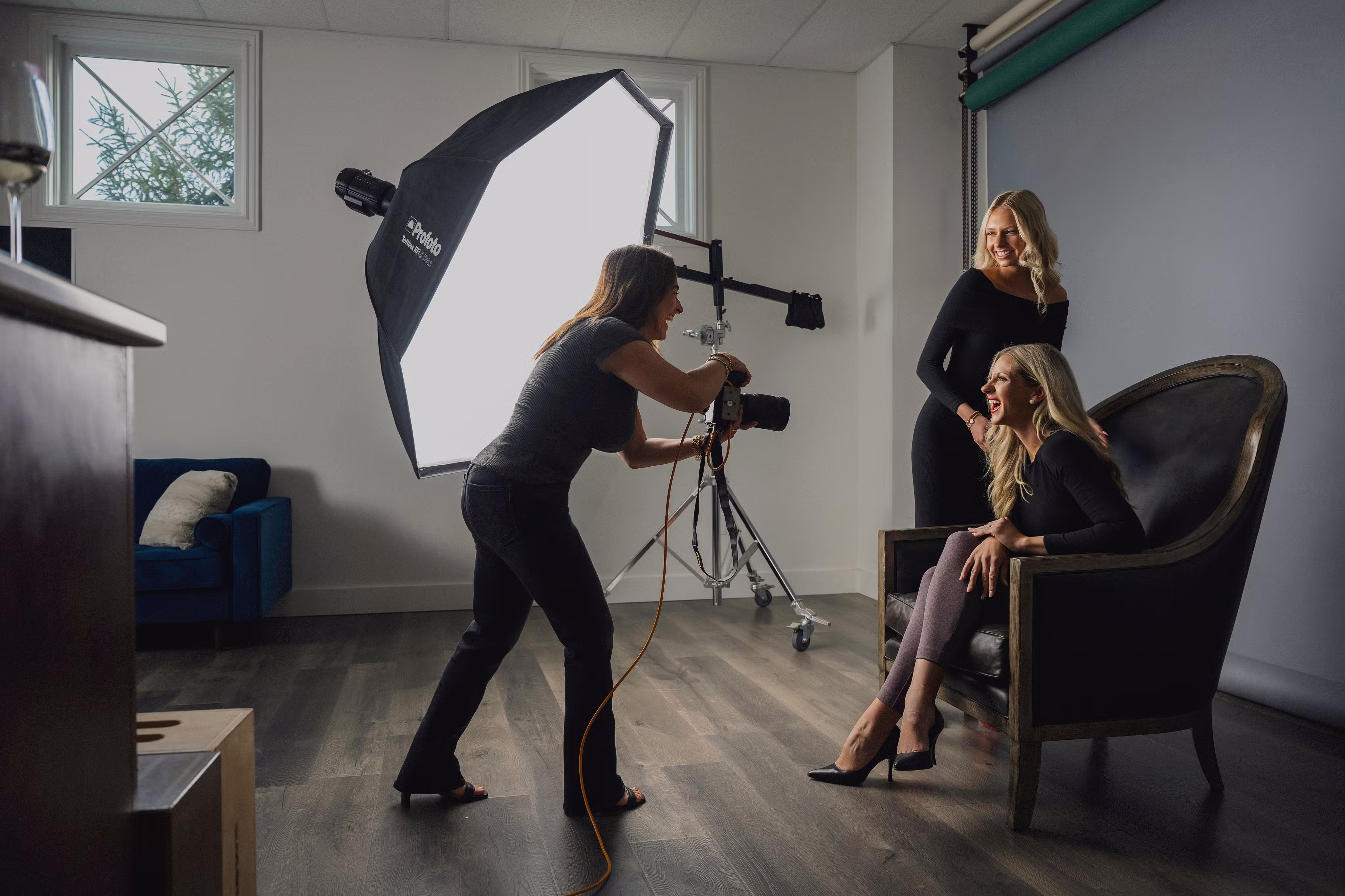 Photographer taking pictures of two smiling women posing in a photography studio with softbox lighting.