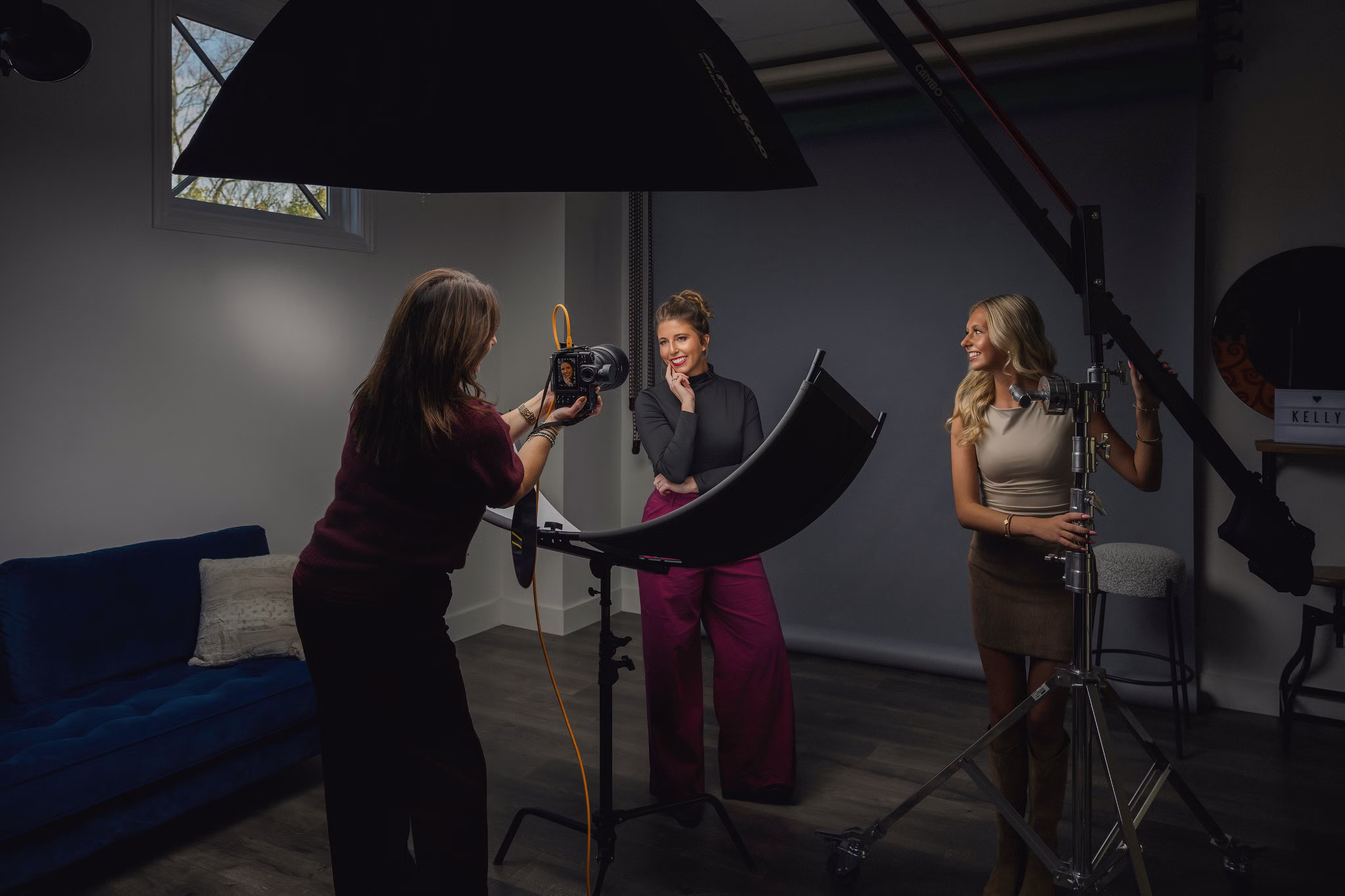 Photographer taking a portrait of a woman posing with hand on chin in a studio while an assistant adjusts lighting equipment.