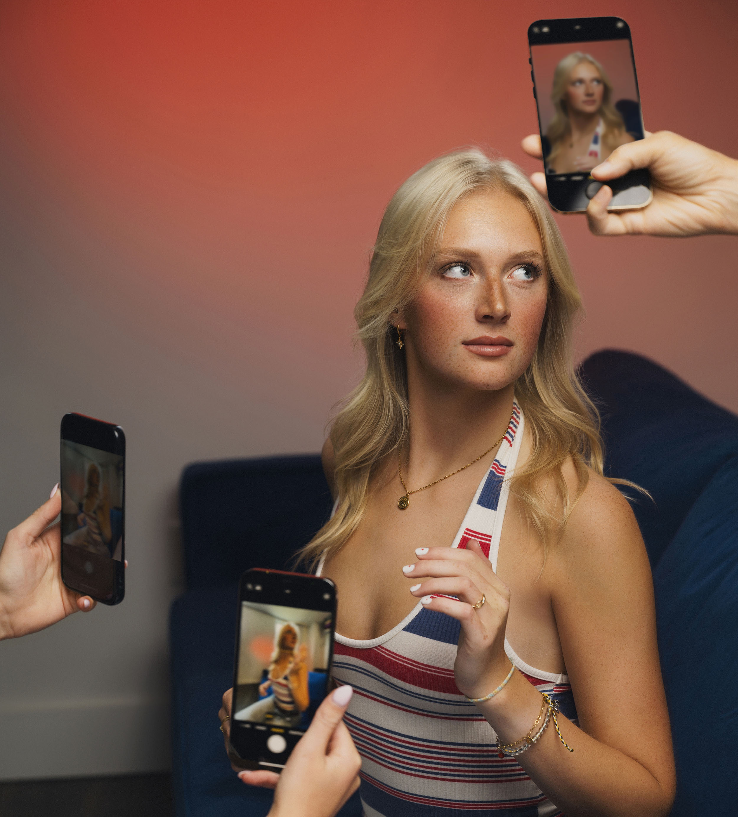 Blonde woman in a striped halter top posing while three smartphones capture her image from different angles.
