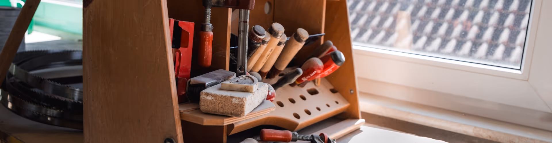 Wooden tool organizer on a windowsill holding various woodworking tools including chisels and clamps.