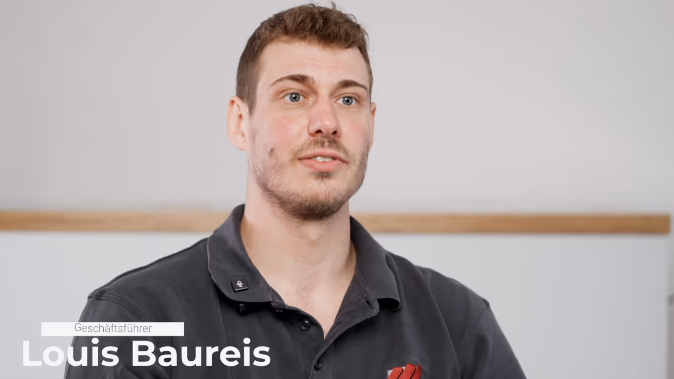 Portrait of a man with short brown hair and beard wearing a dark gray collared shirt against a plain background.