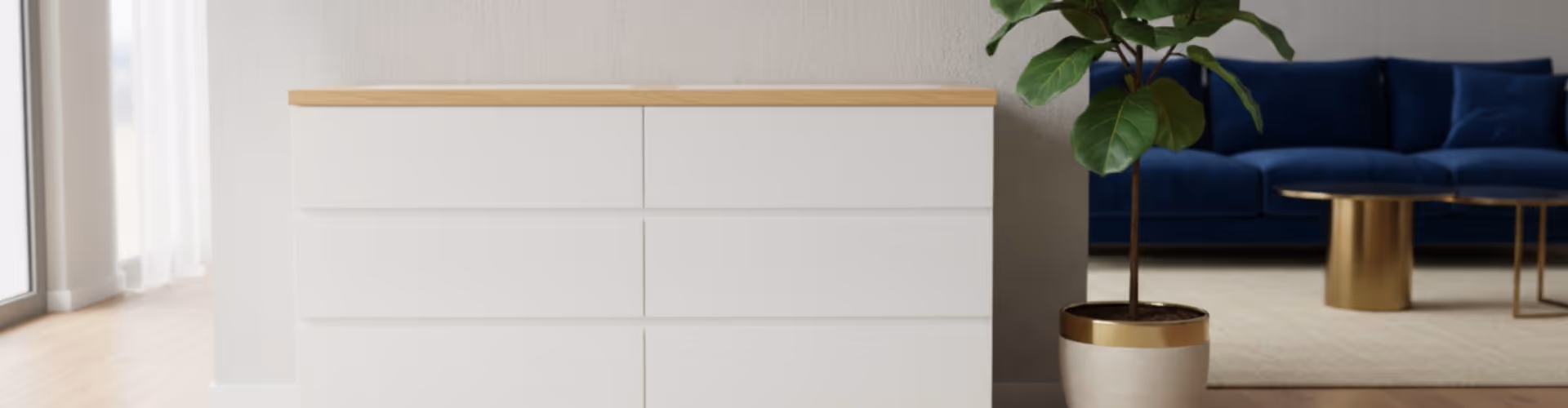 Modern white dresser with light wooden top next to a potted plant, with a blue sofa and gold coffee tables in the background.