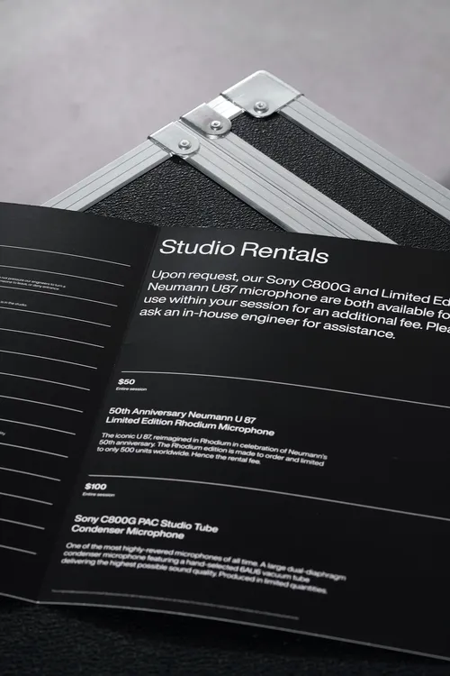 Open booklet titled 'Studio Rentals' detailing rental fees and descriptions for Neumann U87 and Sony C800G microphones on a textured black surface.