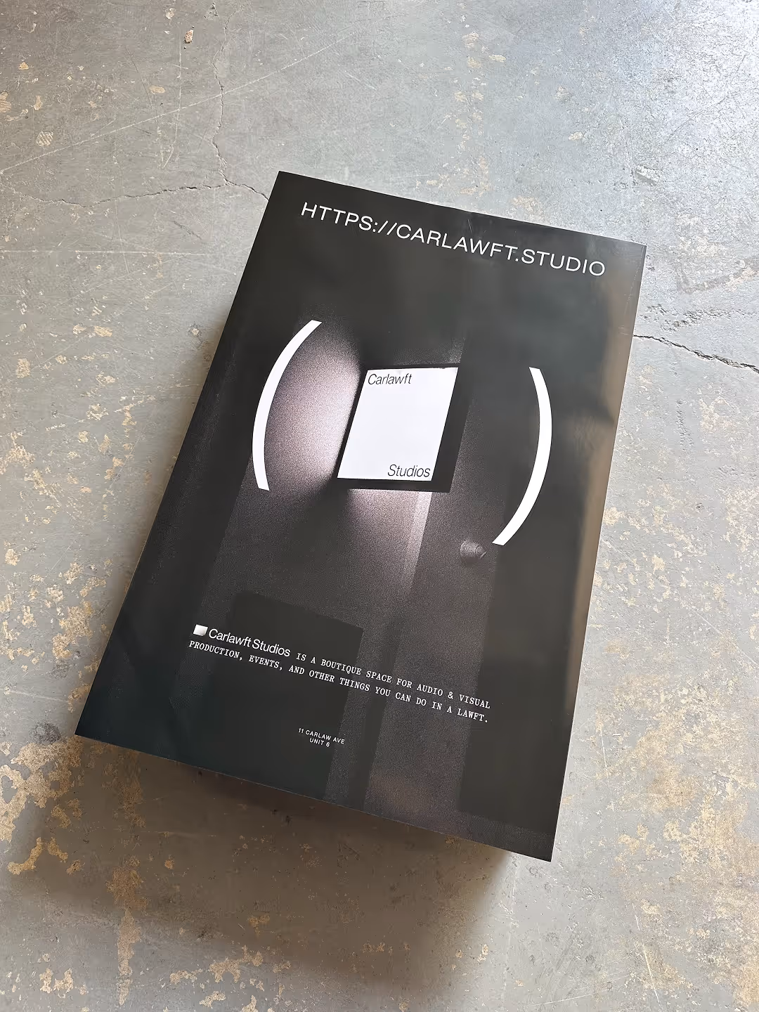 Black poster for Carlawft Studios, describing it as a boutique space for audio and visual production, placed on a worn concrete floor.