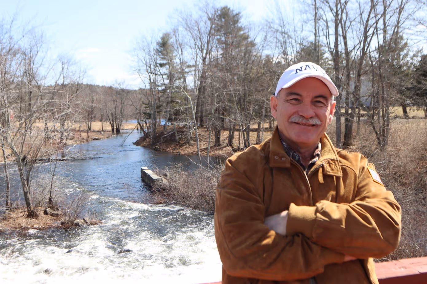 Smiling man wearing a brown jacket and white Navy cap.