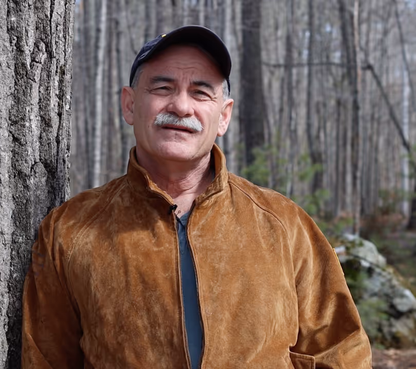 Older man with a mustache wearing a brown jacket and black cap.