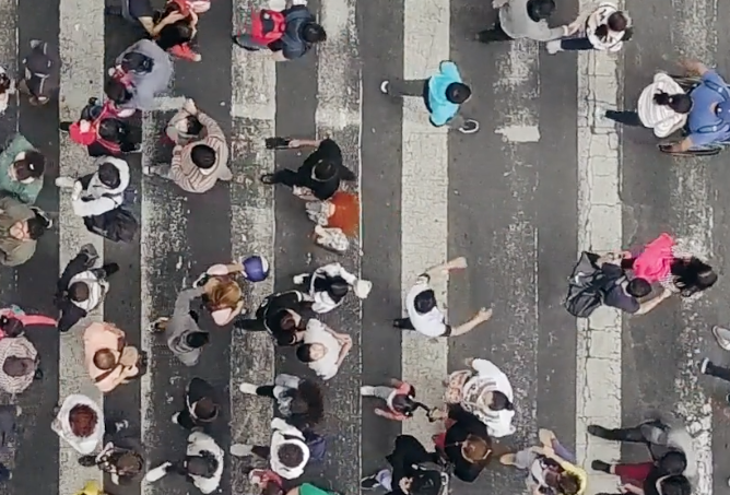 Aerial view of a busy crosswalk with diverse pedestrians moving in various directions.