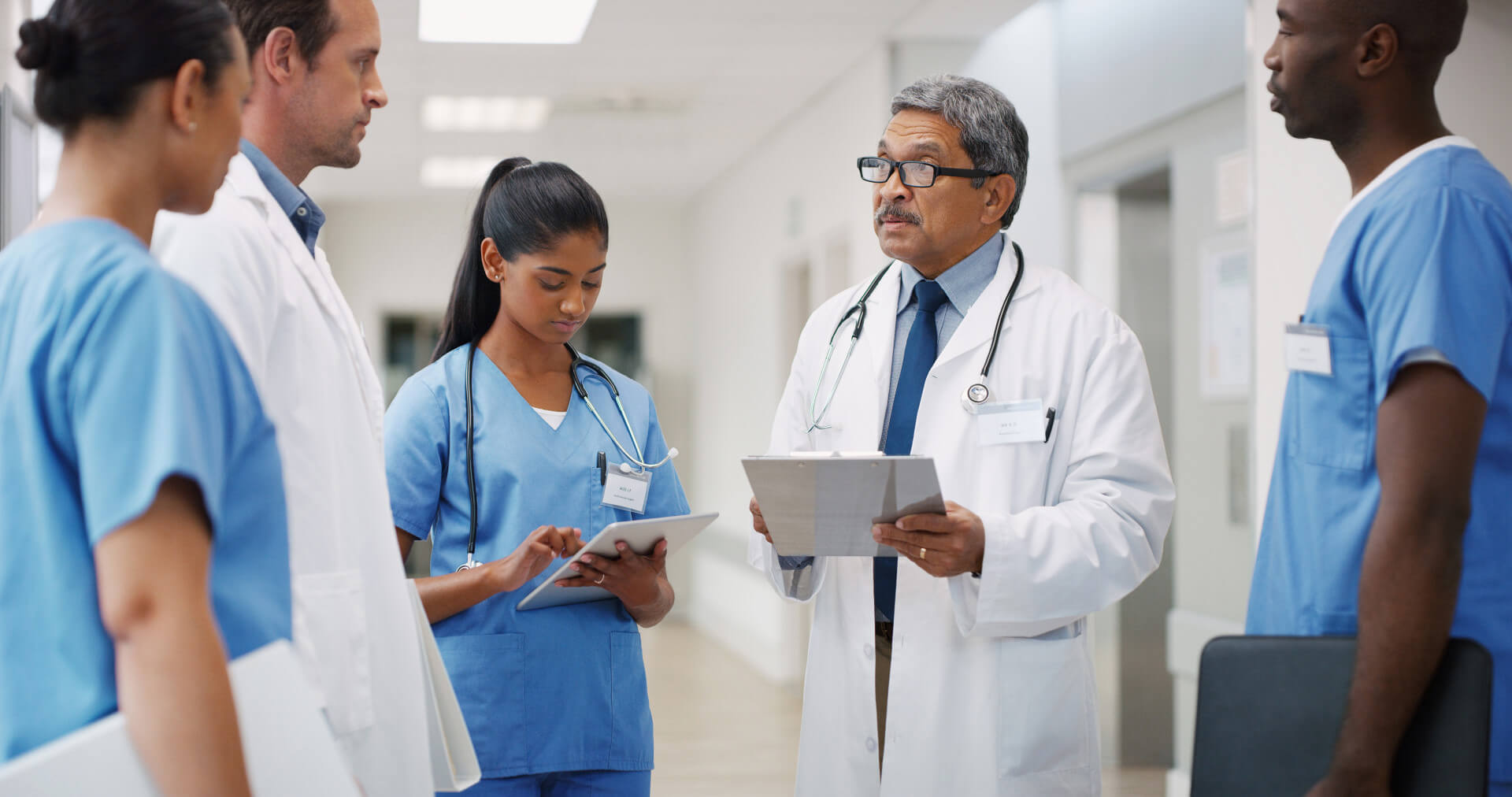 A diverse team of healthcare professionals discussing a patient's care in a hospital corridor.