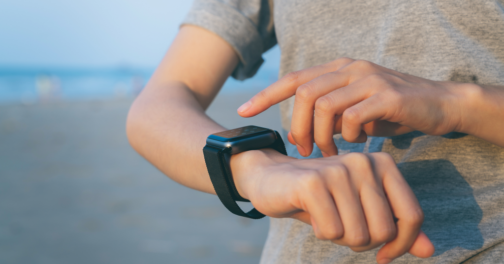 A person interacting with a smartwatch on their wrist while at the beach.