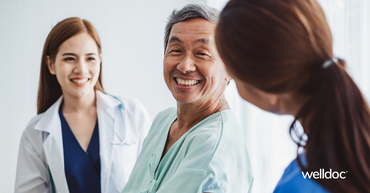 A smiling middle-aged man in patient attire talks with two healthcare professionals in a bright