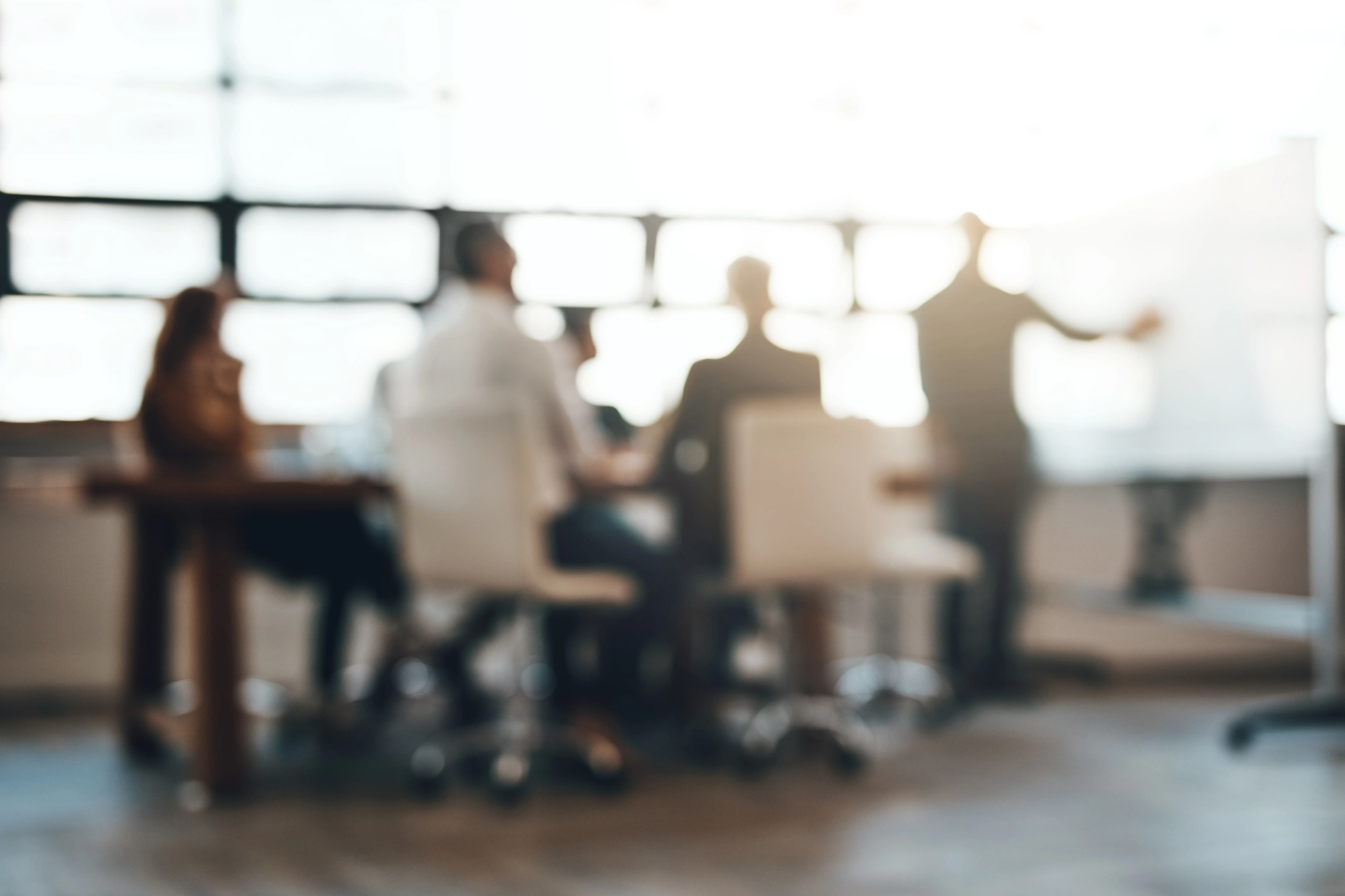 Blurry image of a business meeting with people discussing in front of a whiteboard.