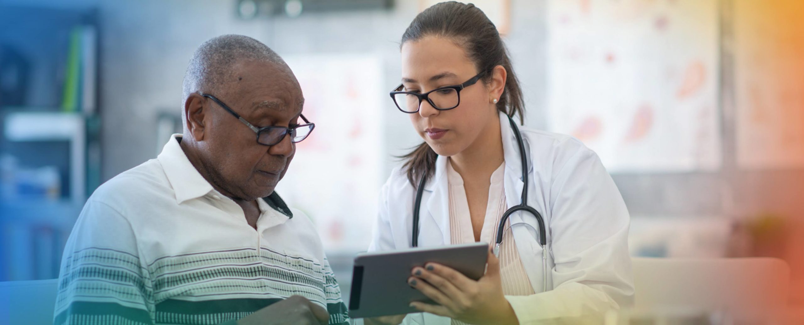 A doctor shows a tablet to an elderly patient during a consultation in a medical setting.