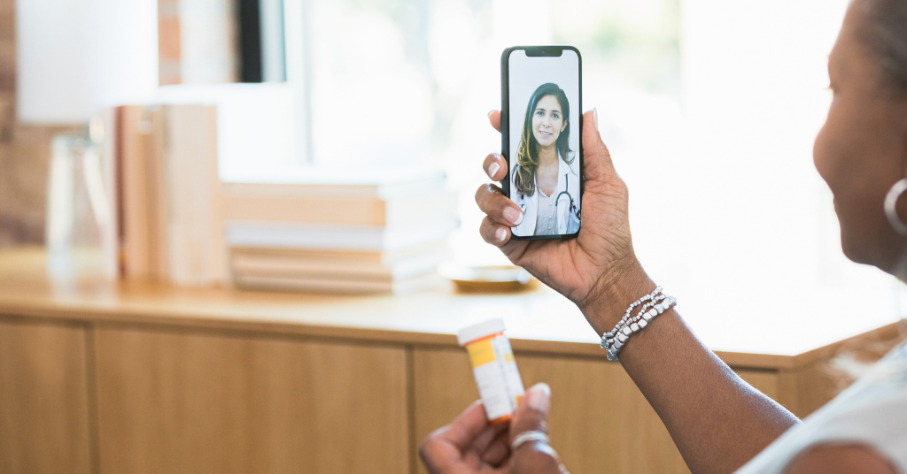 A person holds a smartphone displaying a doctor during a virtual consultation while holding a