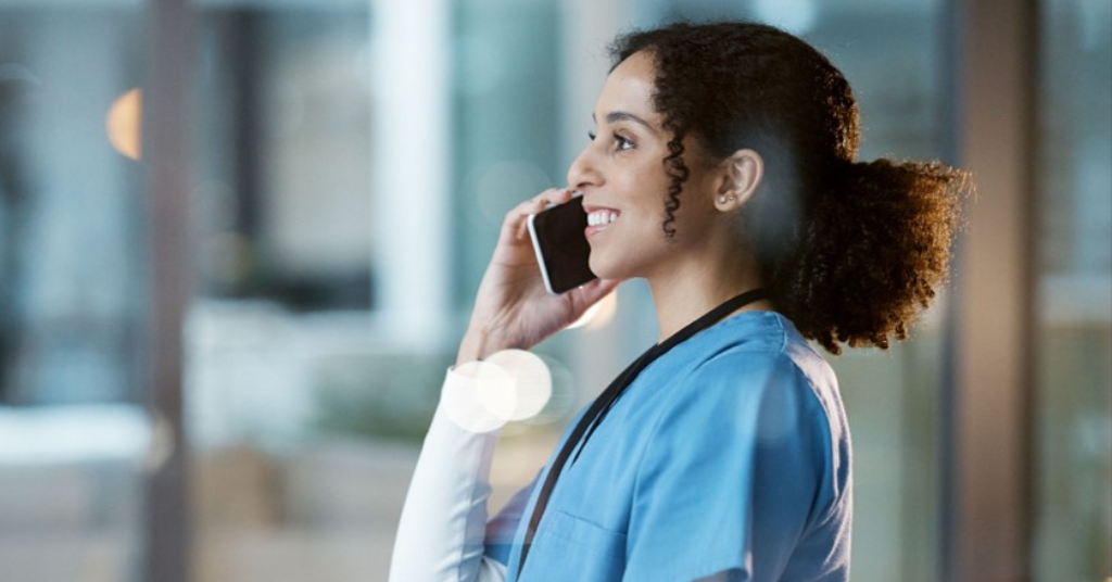 A healthcare professional in scrubs talks on a smartphone, smiling pleasantly.