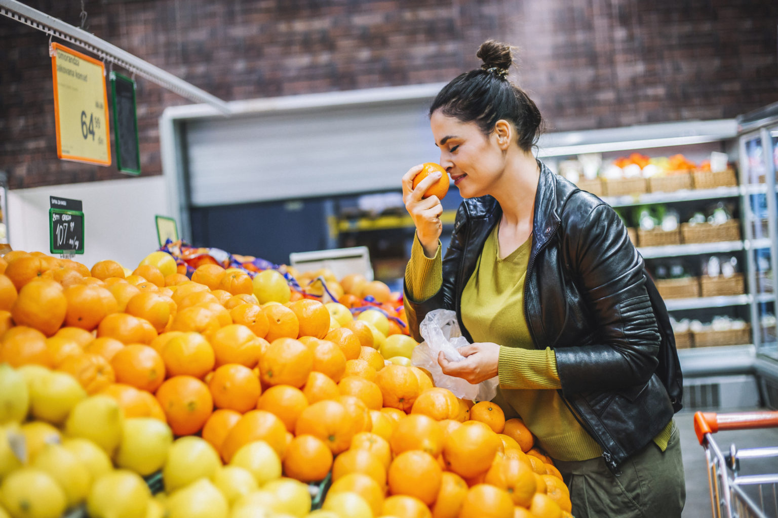 Woman smelling an orange at a grocery store, surrounded by stacks of oranges.