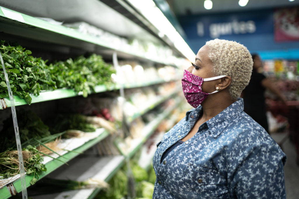 Woman in a mask examines produce on grocery store shelves during COVID-19.