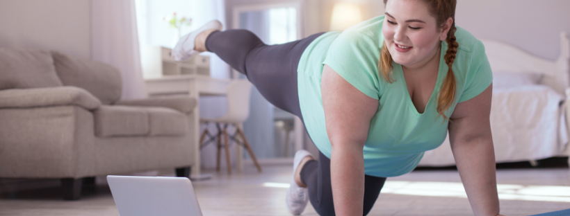 A woman exercises at home, using a laptop for guidance, focusing on her fitness routine.