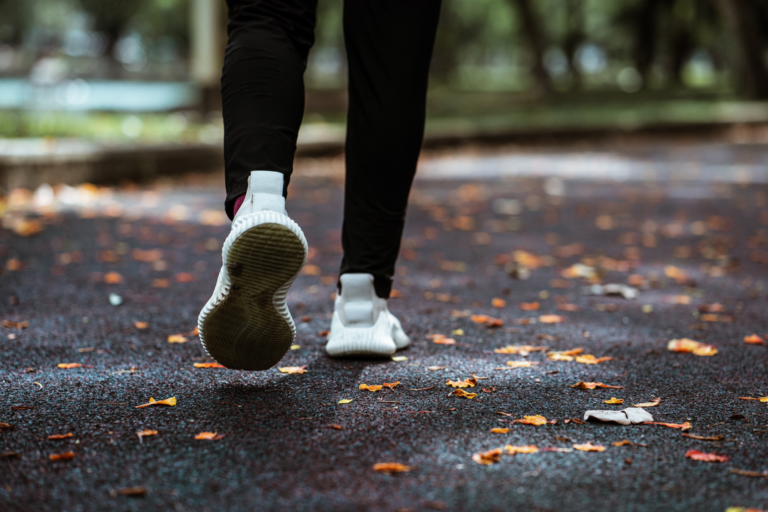 A person jogging on a path covered with autumn leaves, wearing white sneakers.