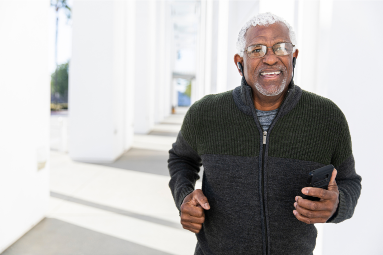 An older man with gray hair jogs outdoors, smiling while holding a smartphone.