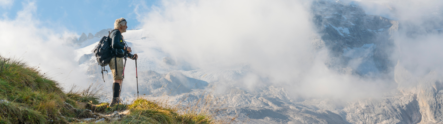 Hiker standing on a grassy slope, with a mountainous landscape and clouds in the background.
