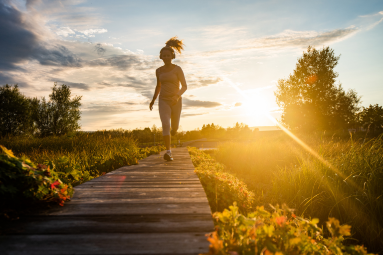 A person jogging on a wooden path during sunset, surrounded by greenery and soft light.