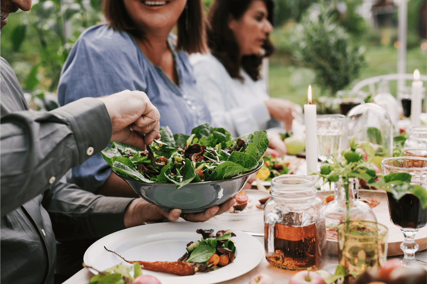 A group enjoying a healthy meal with a large bowl of salad at a garden table setting.