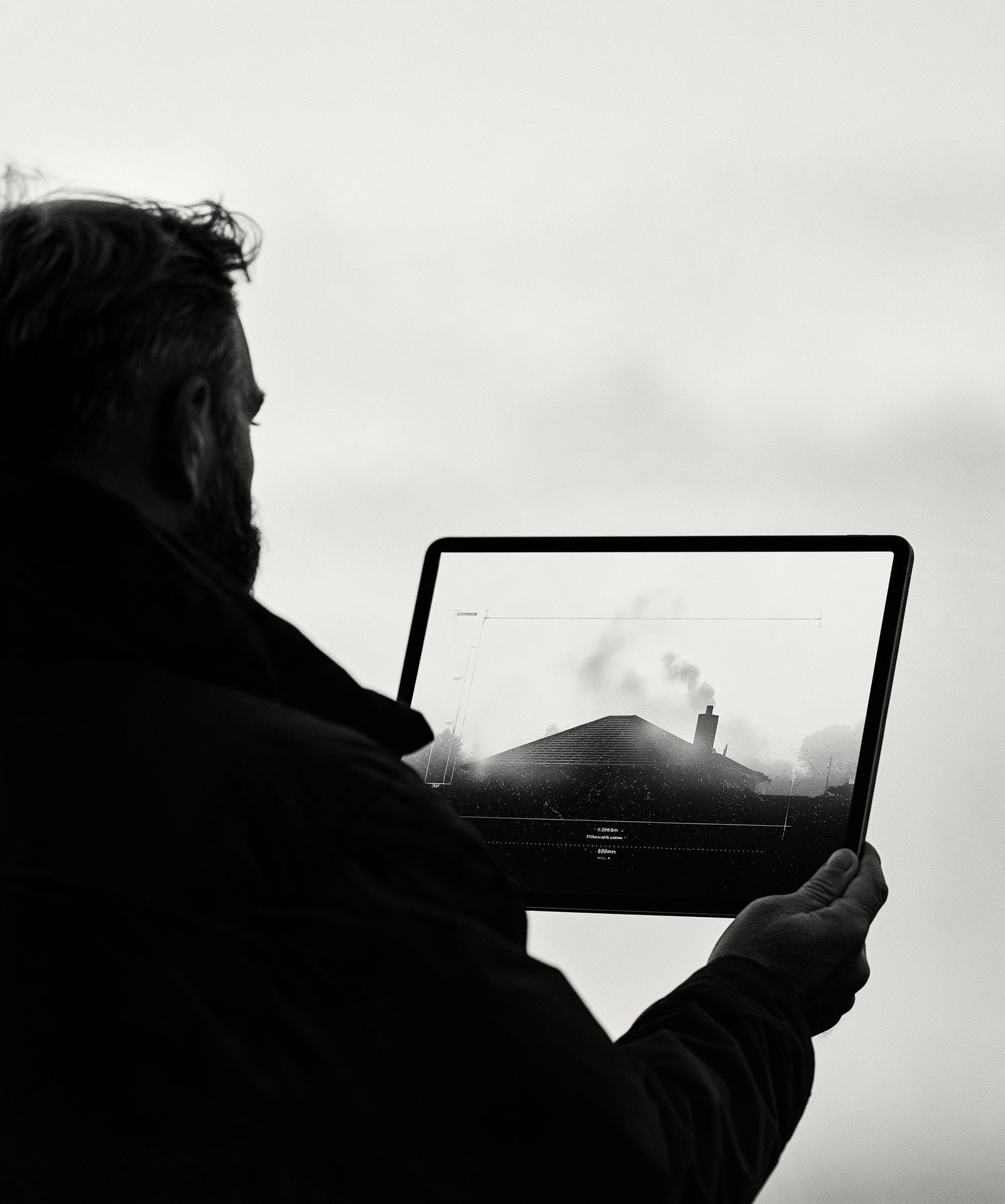 A man holds up a tablet that shows a measured overlay of the roof in front of him