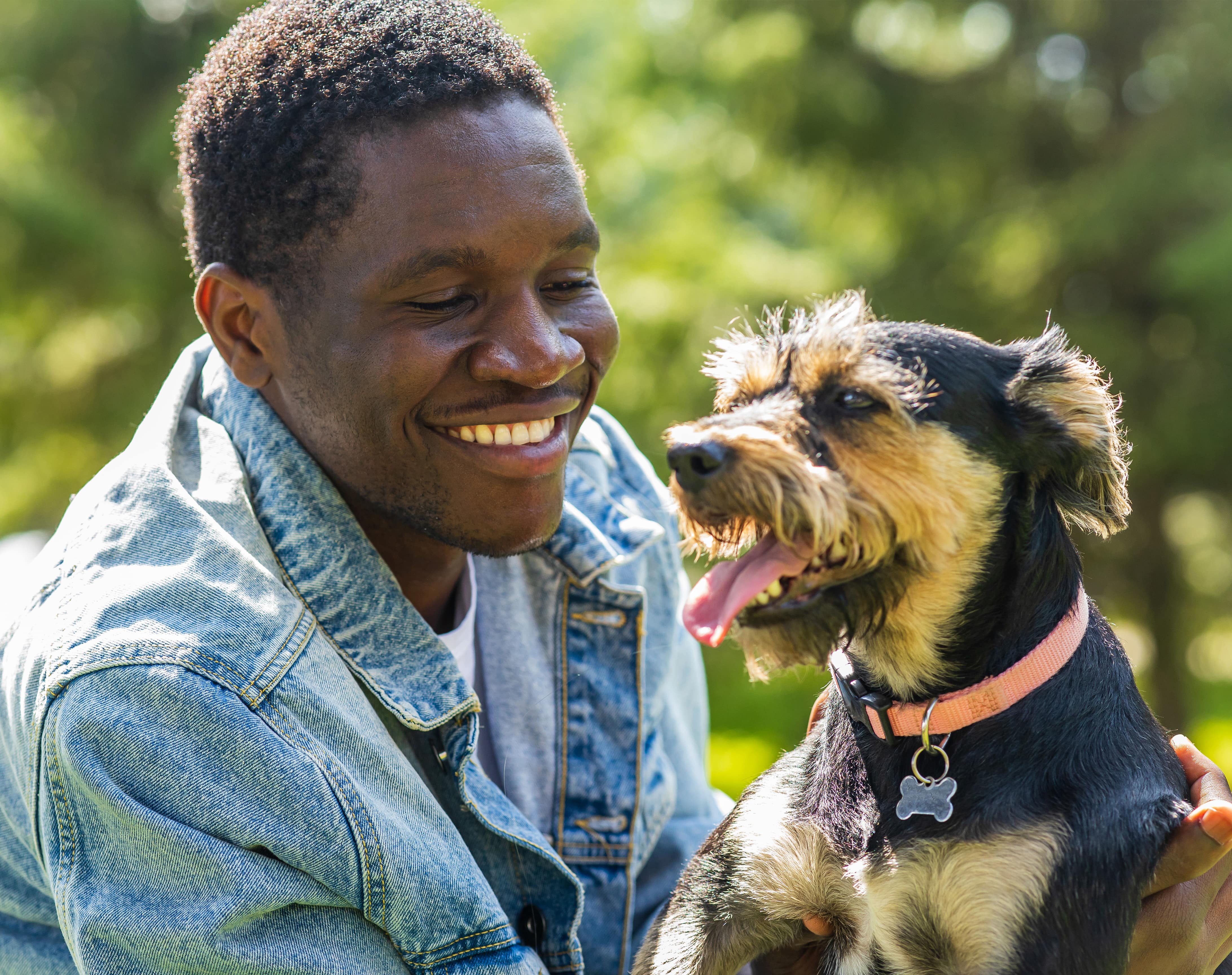 A man smiles next to a small brown and black dog on a summer day