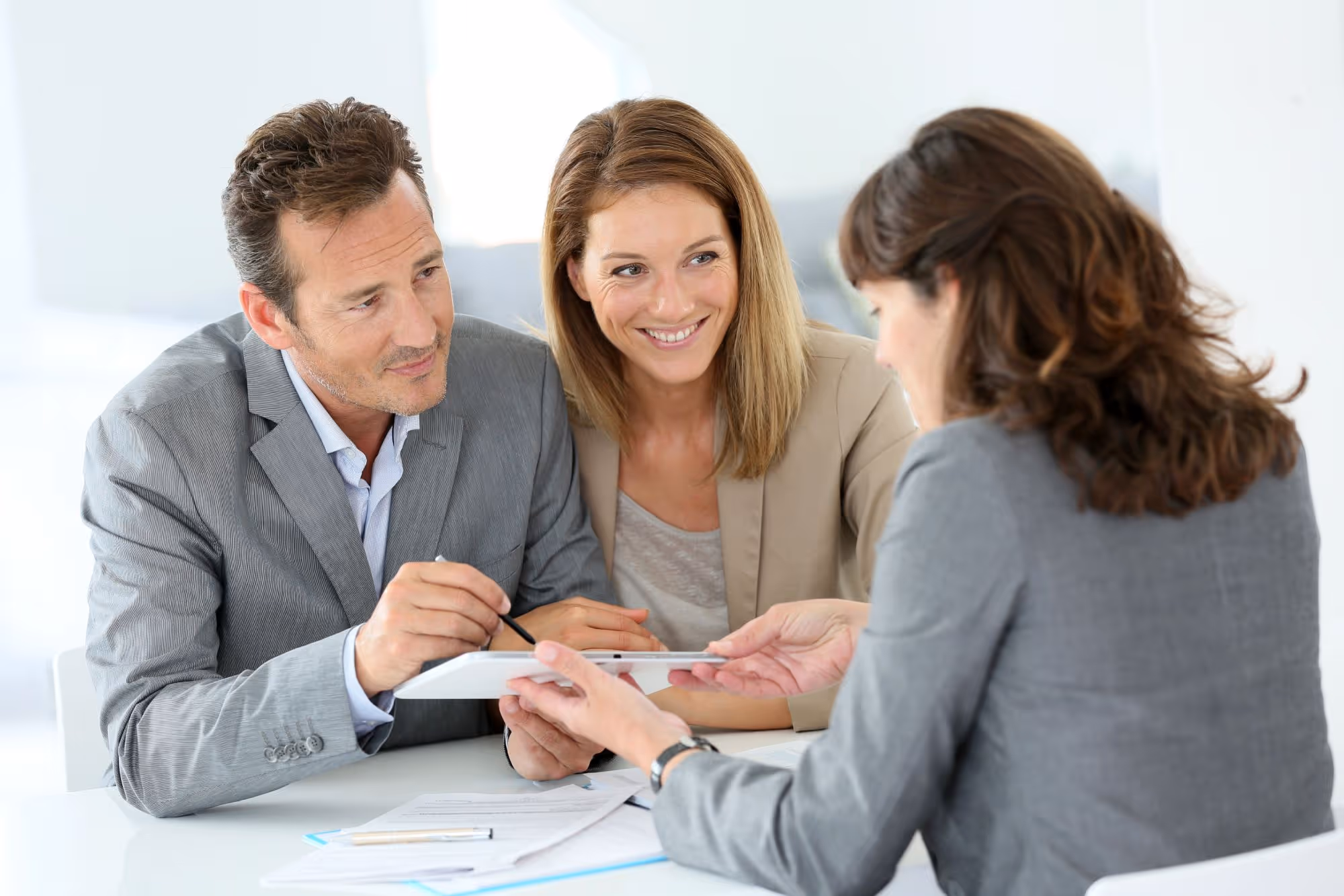A couple reviewing documents and signing on a digital tablet with a professional adviser in an office.