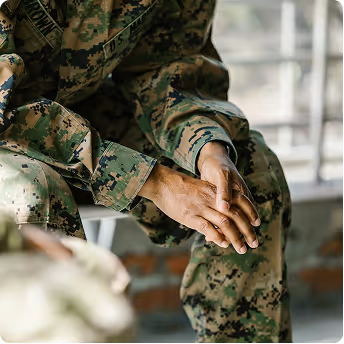 Close-up of a person in camouflage military uniform sitting with hands clasped together.